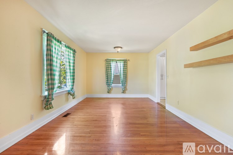 A room with wooden floors and two windows with green curtains.