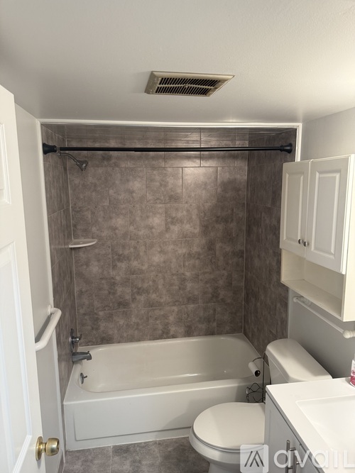 A bathroom with a white tub and toilet, a grey tiled shower, and a white cabinet.