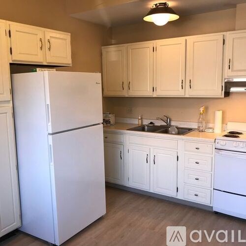 A white refrigerator stands in a kitchen with white cabinets.