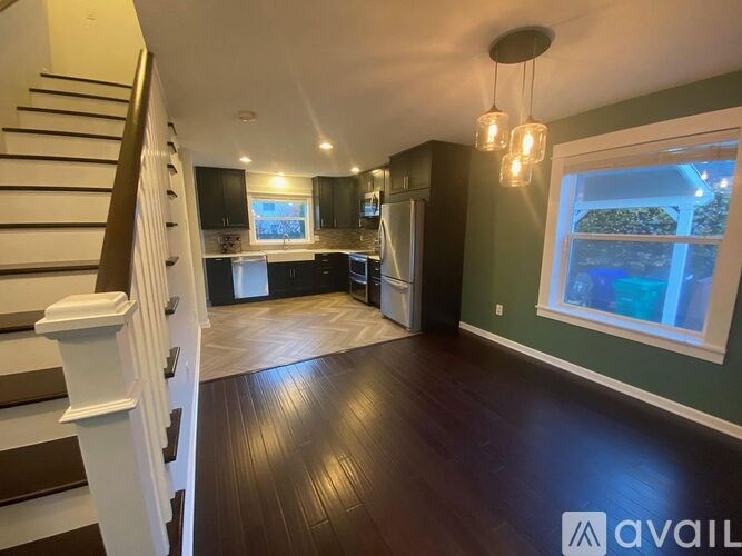 A spacious room with wooden floors and a staircase on the left side.