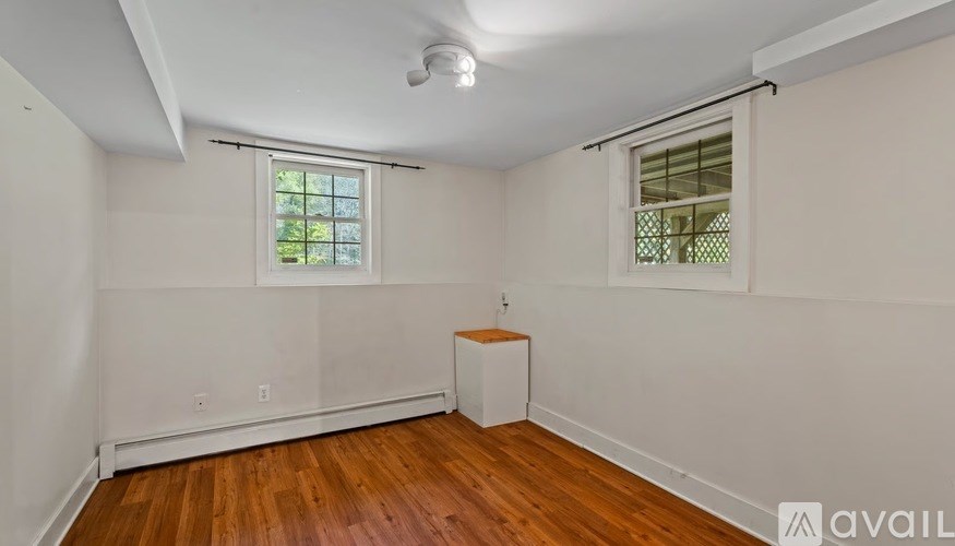 A room with wooden floors and white walls, featuring a window with a view of greenery outside.