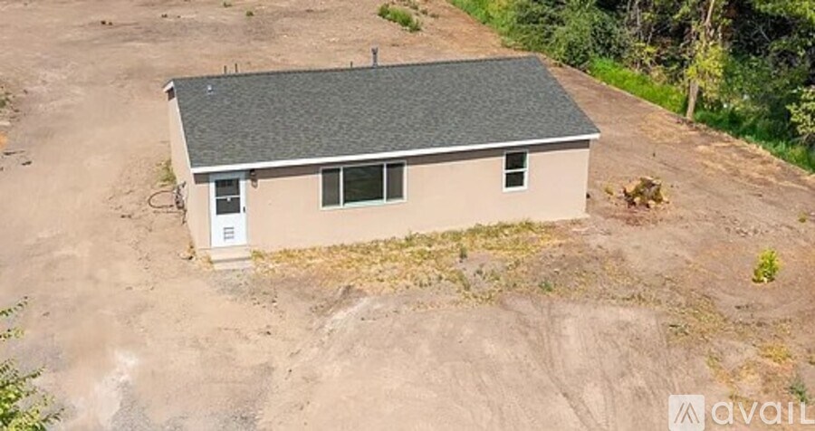 A small house with a grey roof is surrounded by a dirt lot.