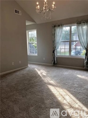 A spacious room with a chandelier, carpeted floor, and large windows with curtains.
