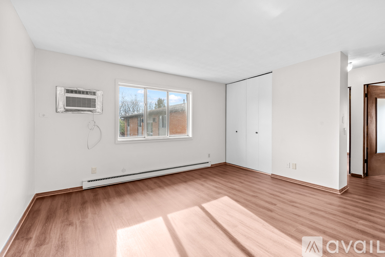 A room with a window, a wall-mounted air conditioner, and a wooden floor.