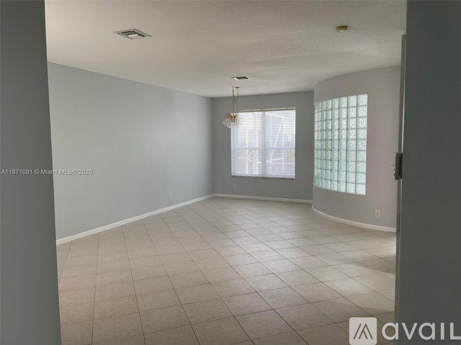 A large empty room with tiled flooring and a window with blinds.
