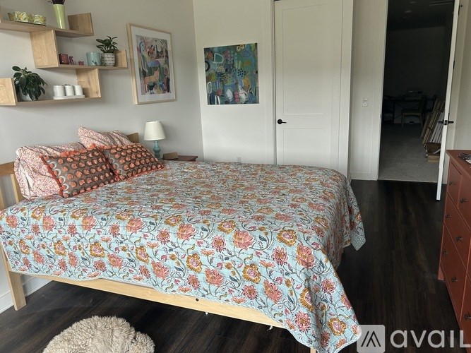 A bed with a floral patterned bedspread sits in a room with a wooden floor and a white door.