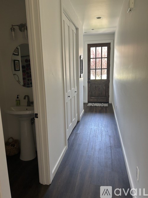 A hallway with a white door and a window with a view of trees.