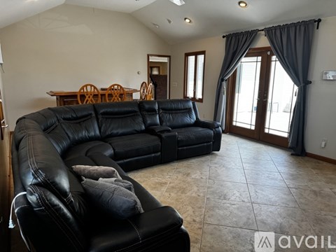 A black leather couch in a spacious living room with a dining table and chairs.
