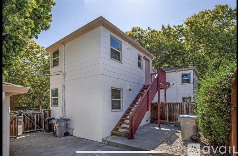 A white house with a red staircase and a brown fence.