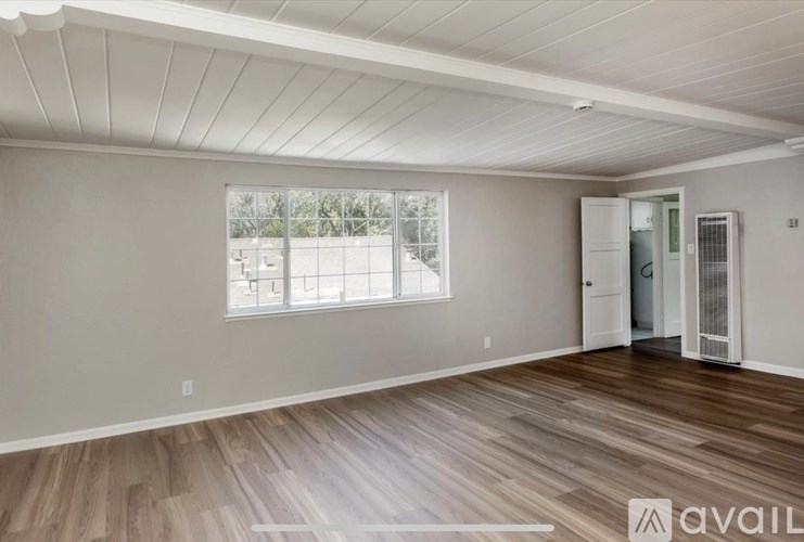 A spacious room with wooden flooring and a large window.