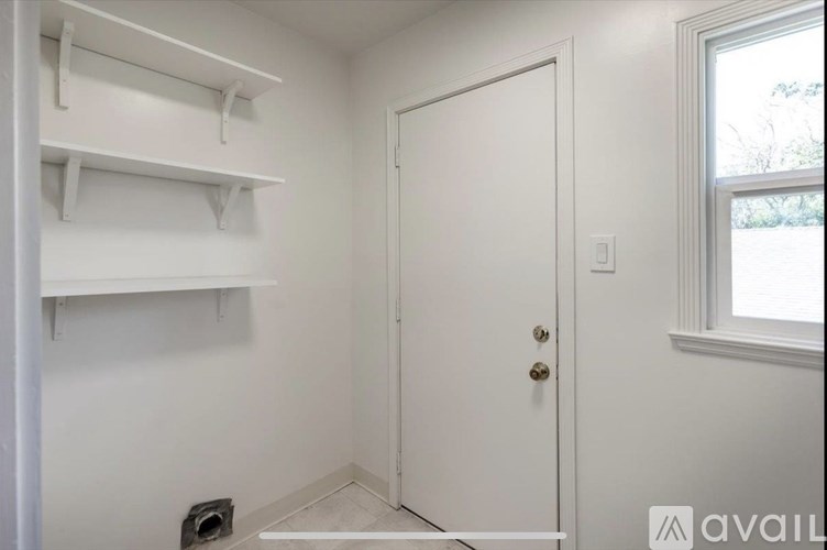 A white door is in a white room with a window and a shelf.