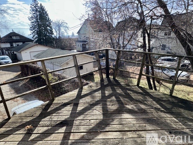 A deck with a railing and a hot tub in the foreground with houses and trees in the background.