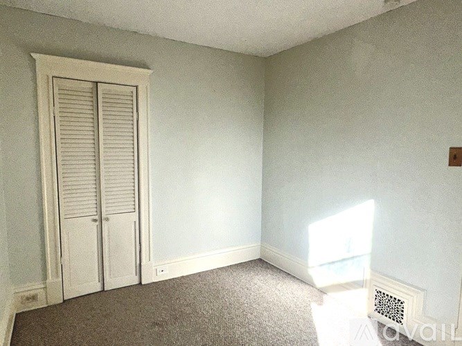 A room with a carpeted floor, a white door with a window on the side, and a vent on the wall.
