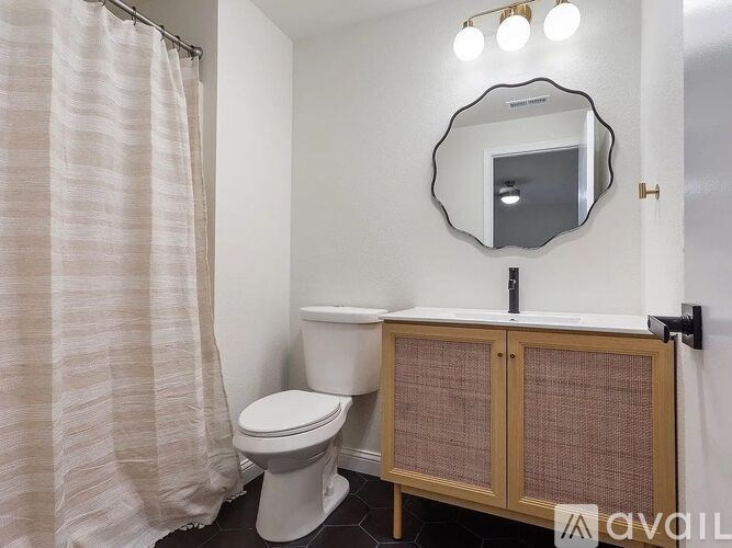 A bathroom with a toilet, a shower curtain, a wooden cabinet and a mirror.