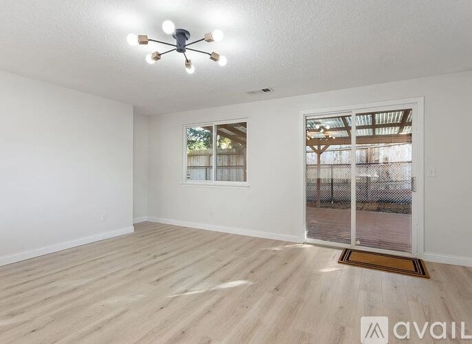 A room with a white wall, wooden floor, and a ceiling fan with lights.