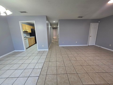 A spacious room with tile flooring and a kitchen visible through an open door.