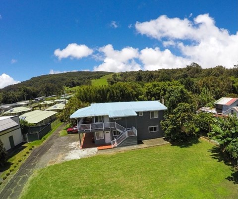 A house with a blue roof is surrounded by greenery and other houses.
