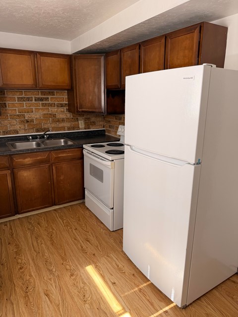 A white refrigerator stands in a kitchen with wooden cabinets and a brick backsplash.