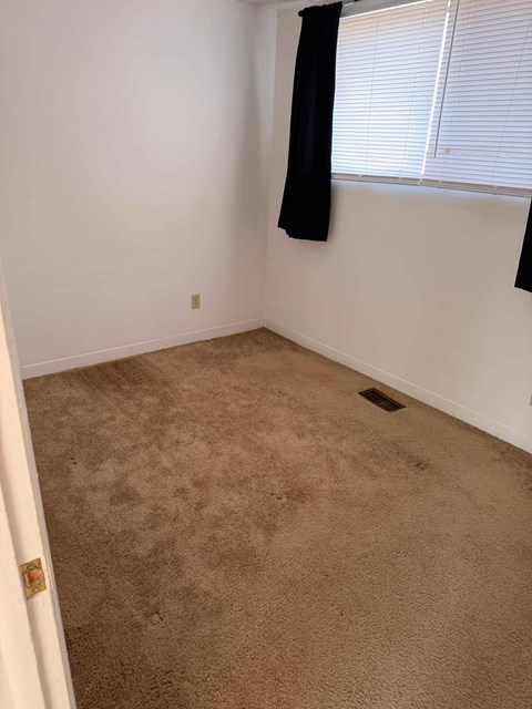 A room with a carpeted floor and a window with blinds.