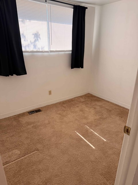 A room with a carpeted floor and a window with blinds.