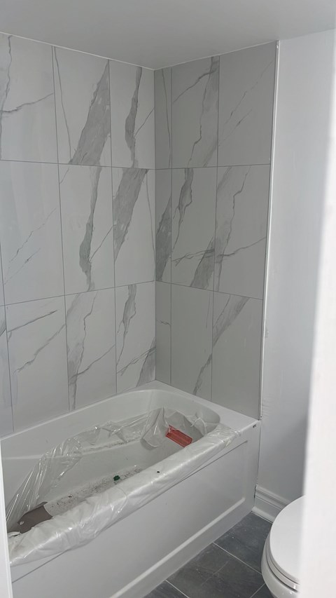 A white bathroom with a marble tile wall and a white bathtub.