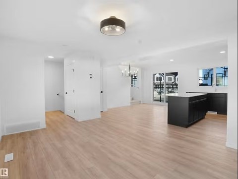 A spacious room with wooden flooring and a kitchen area with black appliances.