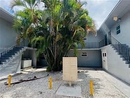 A concrete structure is placed in the middle of a courtyard with a tree and two buildings in the background.