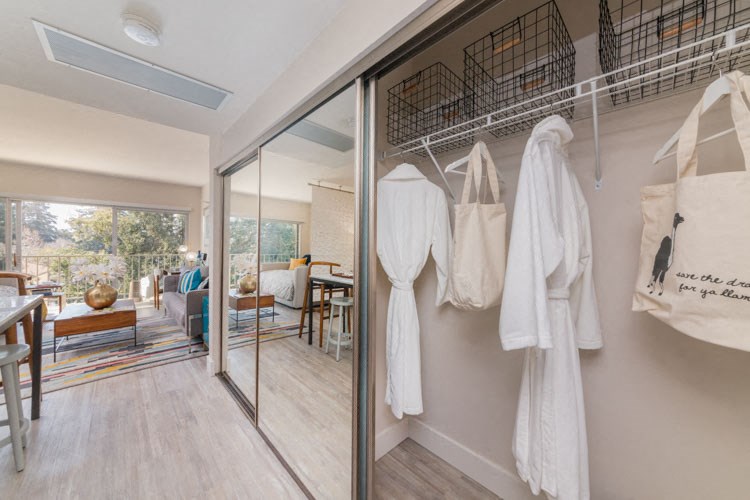 a room with a glass door and a closet with white clothes hanging on the wall