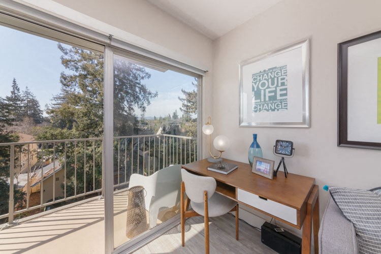 a bedroom with a desk and a large window and a balcony