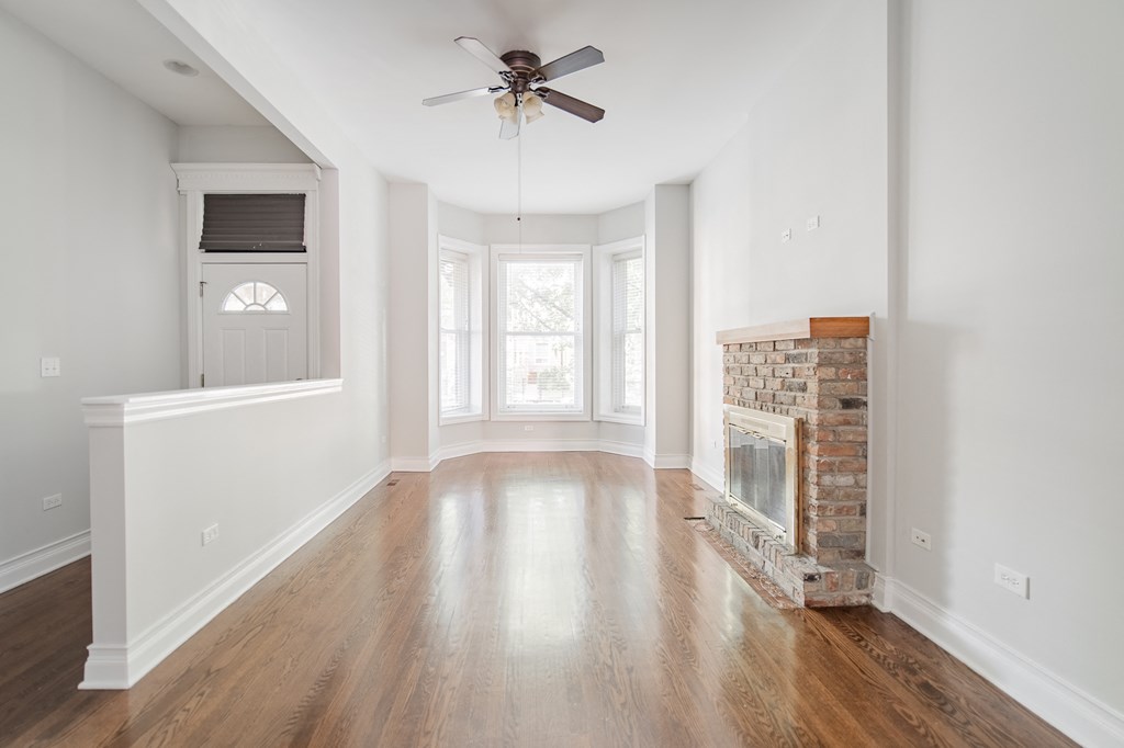an empty living room with a brick fireplace and a ceiling fan