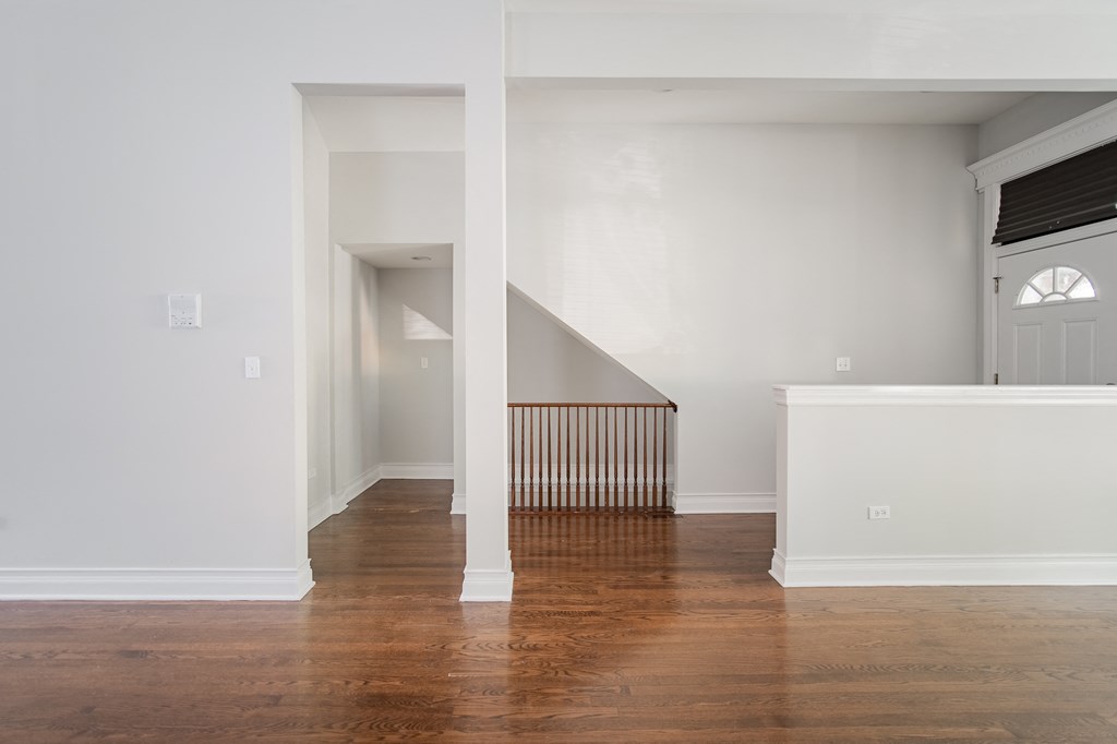 a living room with white walls and a wooden floor and a staircase