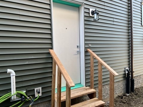 A wooden staircase leads to a white door on a house with a green siding.
