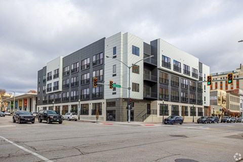 A modern building with a grey and white facade is situated on a street corner with cars parked in front.