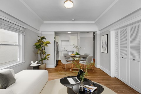 A modern living room with a white sofa, a coffee table with a laptop on it, and a dining area in the background.