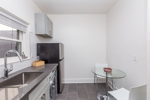 A kitchen with a black refrigerator, a stainless steel sink, and a glass table with a red stool.