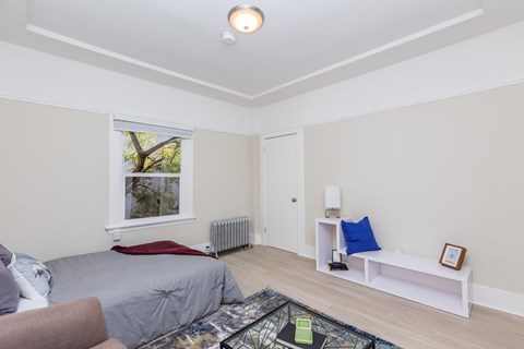 A living room with a grey sofa, a white bench, and a window with a view of trees.