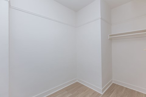 A white room with wooden flooring and a shelf on the wall.