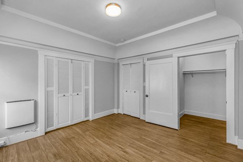 A room with white walls and wooden flooring, furnished with white wardrobes and a white radiator.