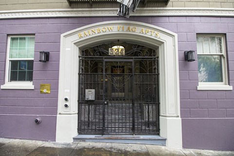 The front of a building with a purple wall and a black gate.