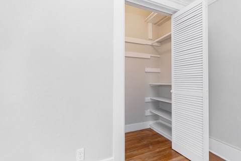 A white shelving unit is open in a room with wood flooring.