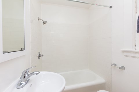A white bathroom with a sink, mirror, and bathtub.