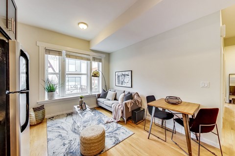A kitchen with a refrigerator on the left and a dining table with chairs in the middle of the room.