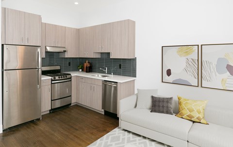 A modern kitchen with a stainless steel refrigerator and a white couch with yellow pillow.