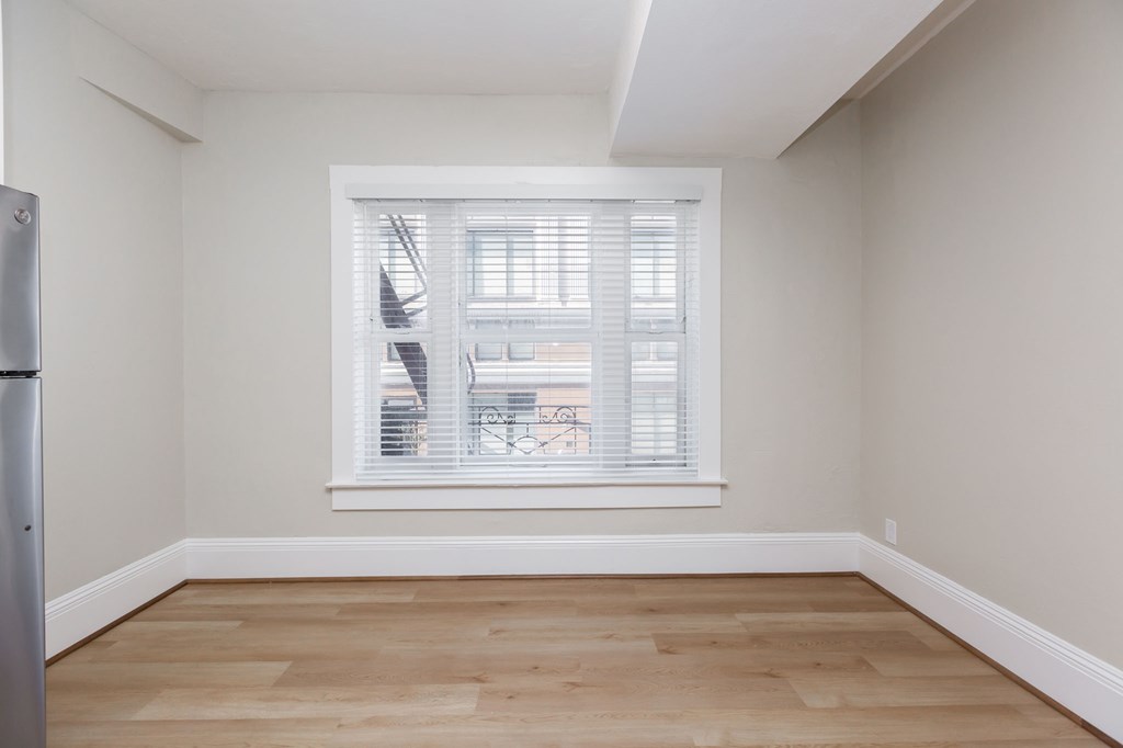 a room with a window and a wooden floor and a refrigerator