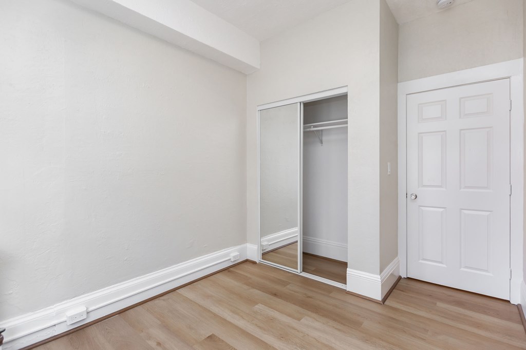 a bedroom with white walls and wood flooring and a closet
