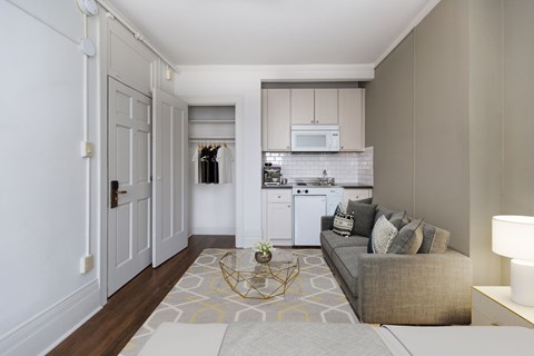 A modern living room with a grey couch and a white kitchen in the background.
