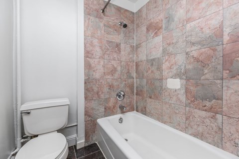 A white toilet sits next to a bathtub in a bathroom with pink marble tiles.
