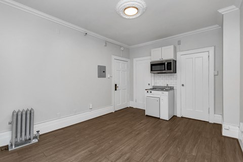 A white kitchen with wood flooring and a microwave above the stove.