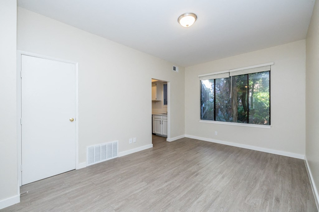 A room with a white door, a window, and a wooden floor.