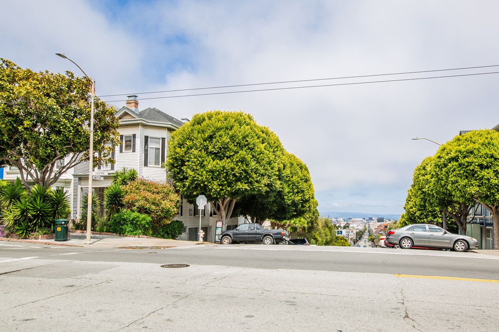 A street view with cars parked on the side of the road and a house in the background.
